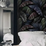 Dark moody bedroom with white pillow and black mirror beside dark tropical palm and banana leaf wallpaper