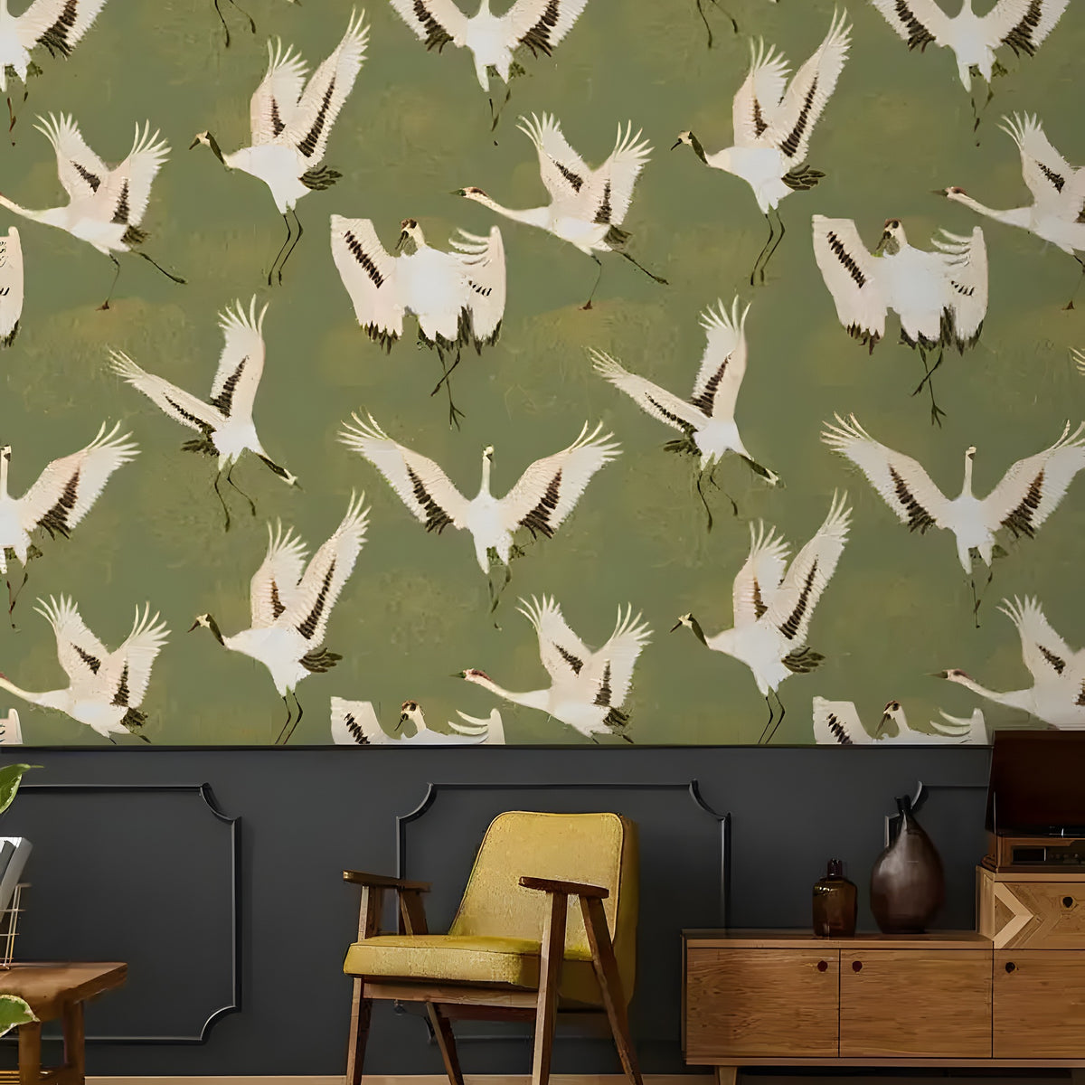Watercolor cranes chinoiserie wallpaper — olive green with white cranes in flight above dark grey paneling, yellow armchair nearby