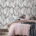 Black and white oversized winter leaves wallpaper in a bedroom with pink bedding, grey throw, and wood floor