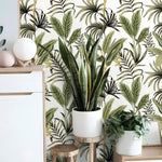 Exotic palm leaf tropical wallpaper in room with white cabinet, potted snake plant on wooden stool