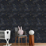Nursery with white crib and gray chair, dark celestial watercolor wallpaper with gold star constellations