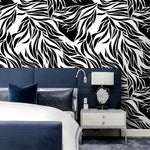 Dramatic abstract leaves black and white wallpaper as headboard wall behind navy upholstered bed with silver nightstand and agate lamp