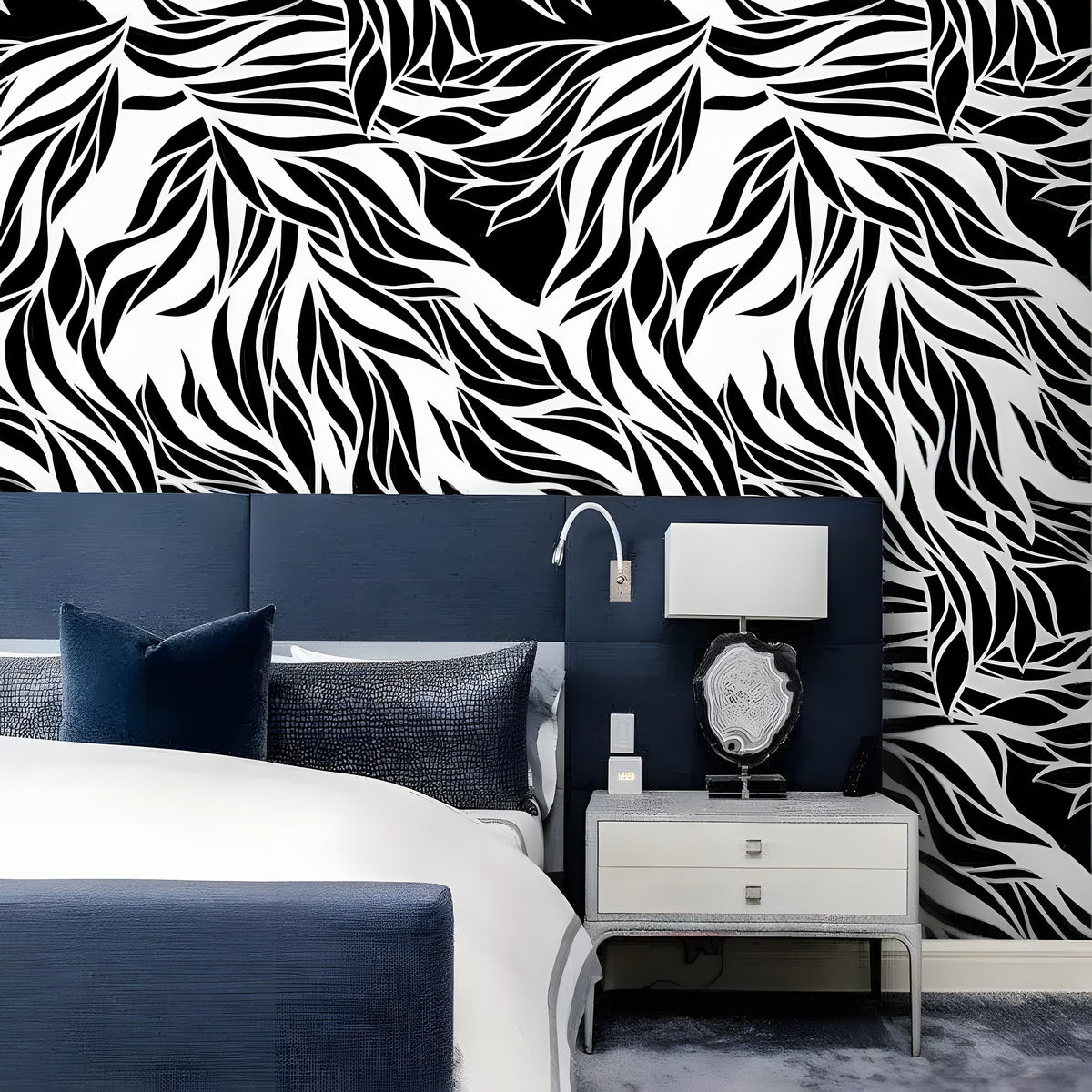 Dramatic abstract leaves black and white wallpaper as headboard wall behind navy upholstered bed with silver nightstand and agate lamp