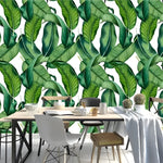 Dining table with white runner and cactus; green and white banana leaves tropical wallpaper with large dark green overlapping leaves