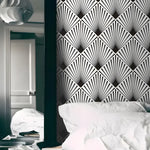 Black and white edgy art deco fan wallpaper as headboard wall behind white bed with stacked books and pendant lamp