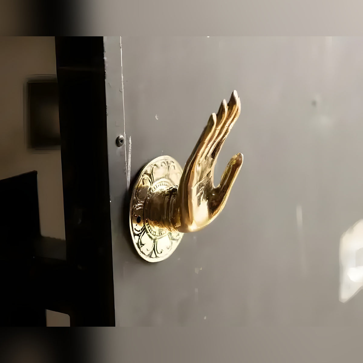 Polished brass Shuni Mudra Buddha hand door knob on grey door, fingers pointing up on engraved round backplate