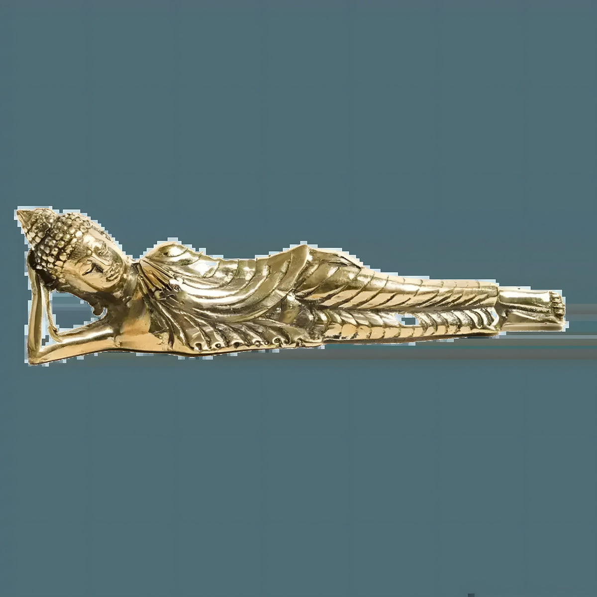Gold brass reclining Buddha figurine, full side view on light gray surface, head resting on arm, detailed robes