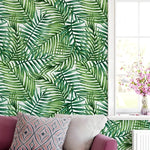 Watercolor tropical green palm leaves wallpaper on wall behind mauve sofa with pink floral cushion
