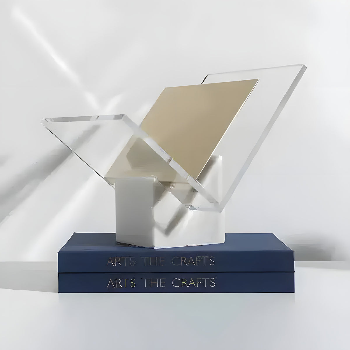 Marble and acrylic magazine rack with clear X-shaped acrylic panels on a white marble cube base atop navy books