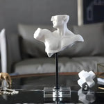 White male torso bust on a black stem and clear acrylic base displayed on a marble coffee table