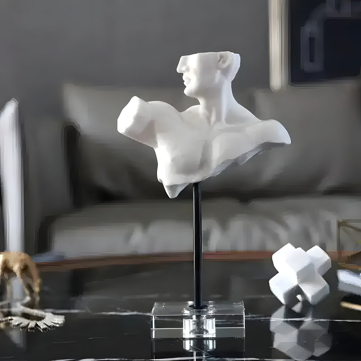 White male torso bust on a black stem and clear acrylic base displayed on a marble coffee table