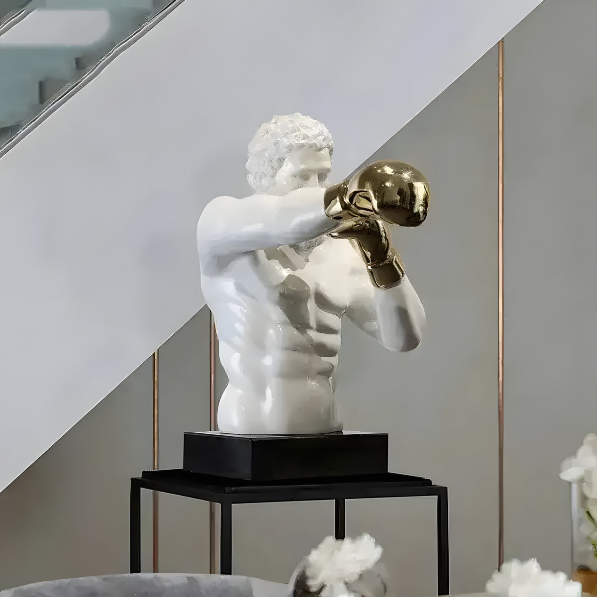 Grand boxing man statue with golden gloves in fighting stance on black metal pedestal in room setting