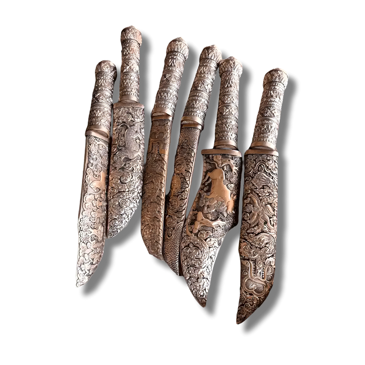 Multiple hand-engraved Khmer knives fanned out, ornate brass handles and blades with traditional Khmer motifs