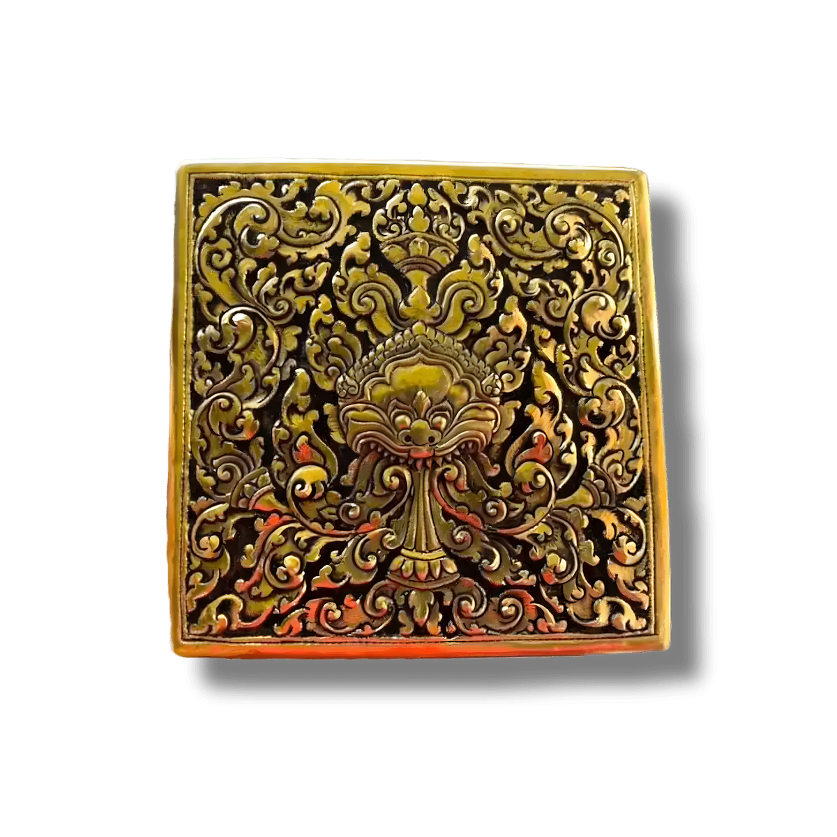 Square brass niello betel box top view — gold deity face and floral scrollwork on black enamel, orange-red accents