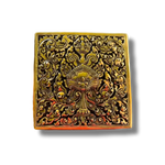 Square brass niello betel box top view — gold deity face and floral scrollwork on black enamel, orange-red accents