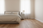 A minimalist bedroom scene with a bed dressed in beige bedding, a small patterned nightstand with a lamp, and light wood flooring against cream walls and sheer curtains.