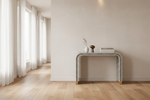 A modern console table with a black and white striped bone-look frame and gold-toned legs, styled with a vase, small sculpture, and books in a bright, minimalist room with light wood floors and sheer curtains.