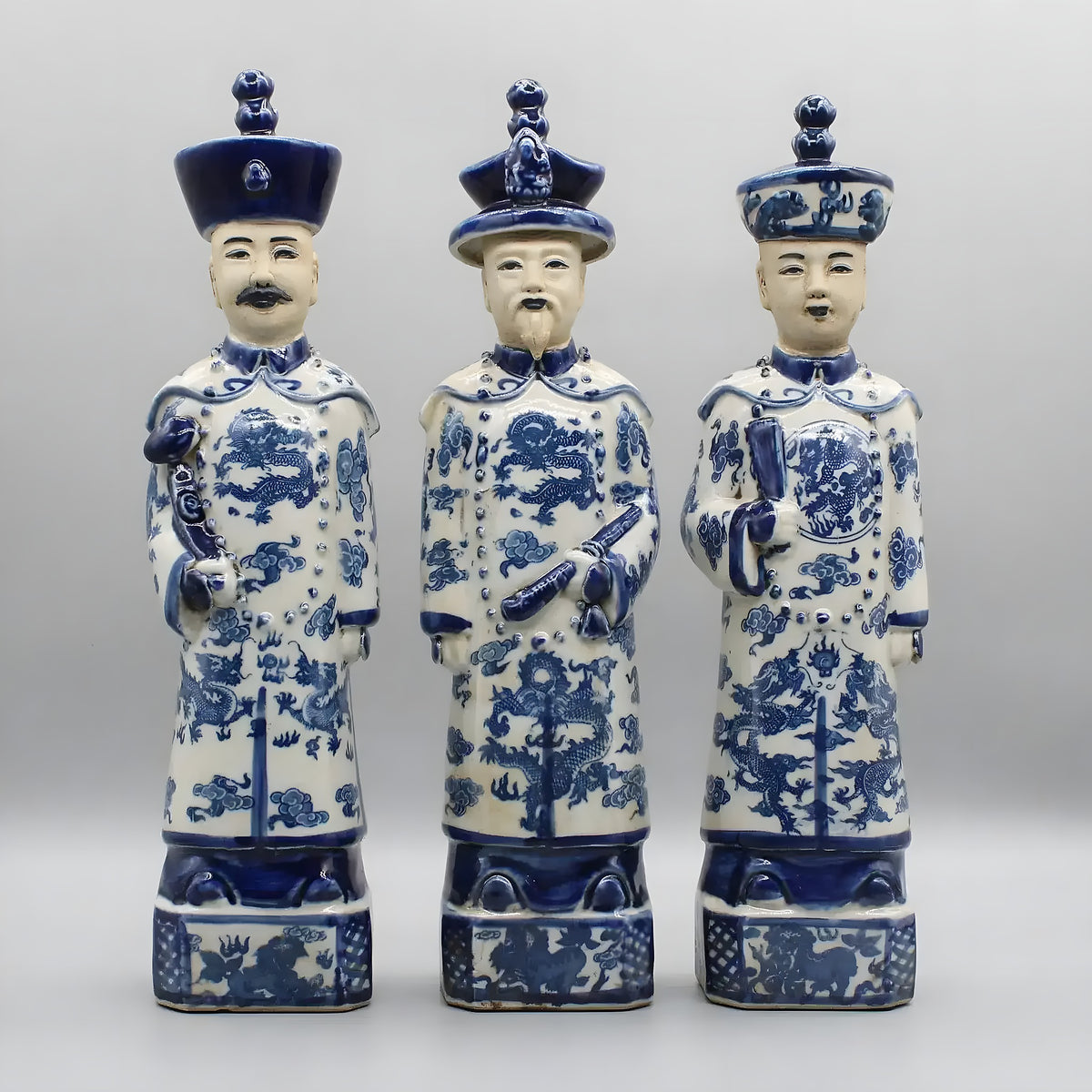 Three blue and white Qing dynasty standing ceramic emperor figurines in dragon-motif robes, front view
