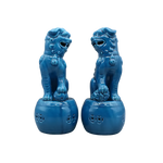 Pair of cerulean blue ceramic foo dog lion sculptures seated on round perforated drum bases, front view, light grey background