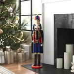 Nutcracker king with cape beside lit Christmas tree — red blue gold uniform with scepter, black boots, pillar candles