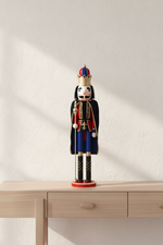 A traditional wooden nutcracker figurine dressed as a king, standing on a light wood console table against a textured off-white wall with soft diagonal shadows.
