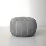Gray leather round Moroccan floral pouf, front view on gray floor, geometric honeycomb stitching