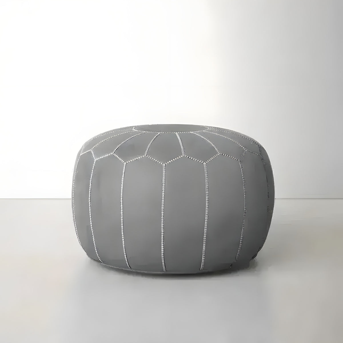 Gray leather round Moroccan floral pouf, front view on gray floor, geometric honeycomb stitching