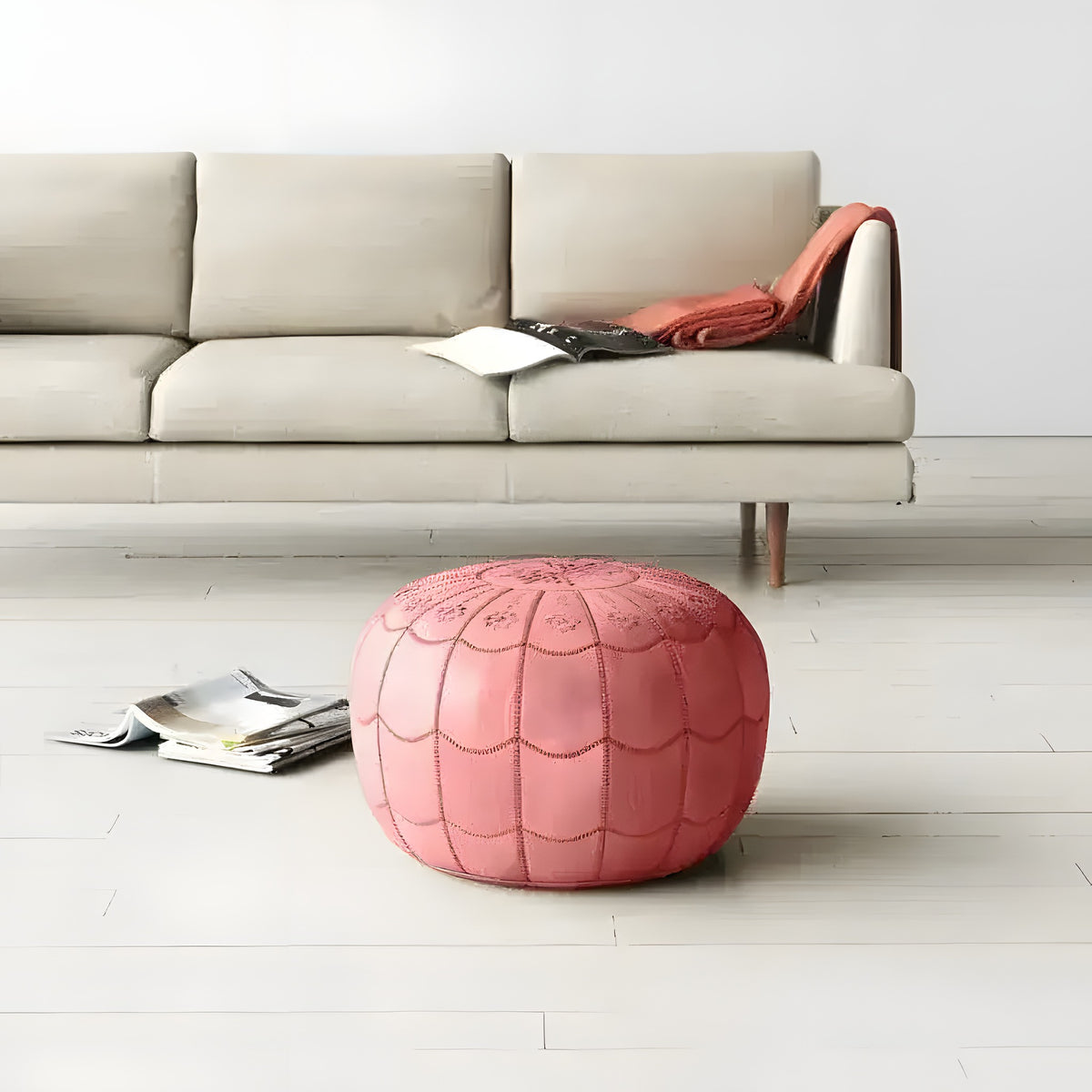 Pink round leather floral pouf ottoman in minimalist living room before a beige sofa, magazine on white floor