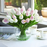 Artificial tulip arrangement in round globe glass vase, mixed white and blush pink tulips, styled on white table with open book