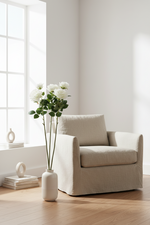 Artificial rose stems with white blooms in a tall vase beside a cream armchair.