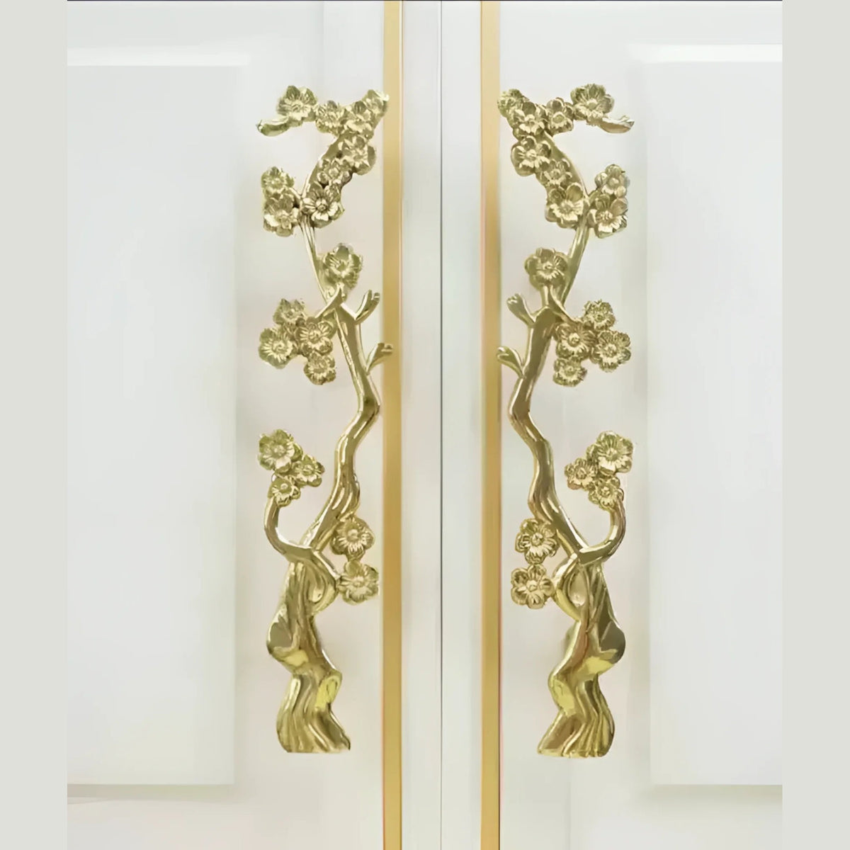 Pair of gold cherry blossom branch door handles on adjacent white cabinet panels, front-facing view