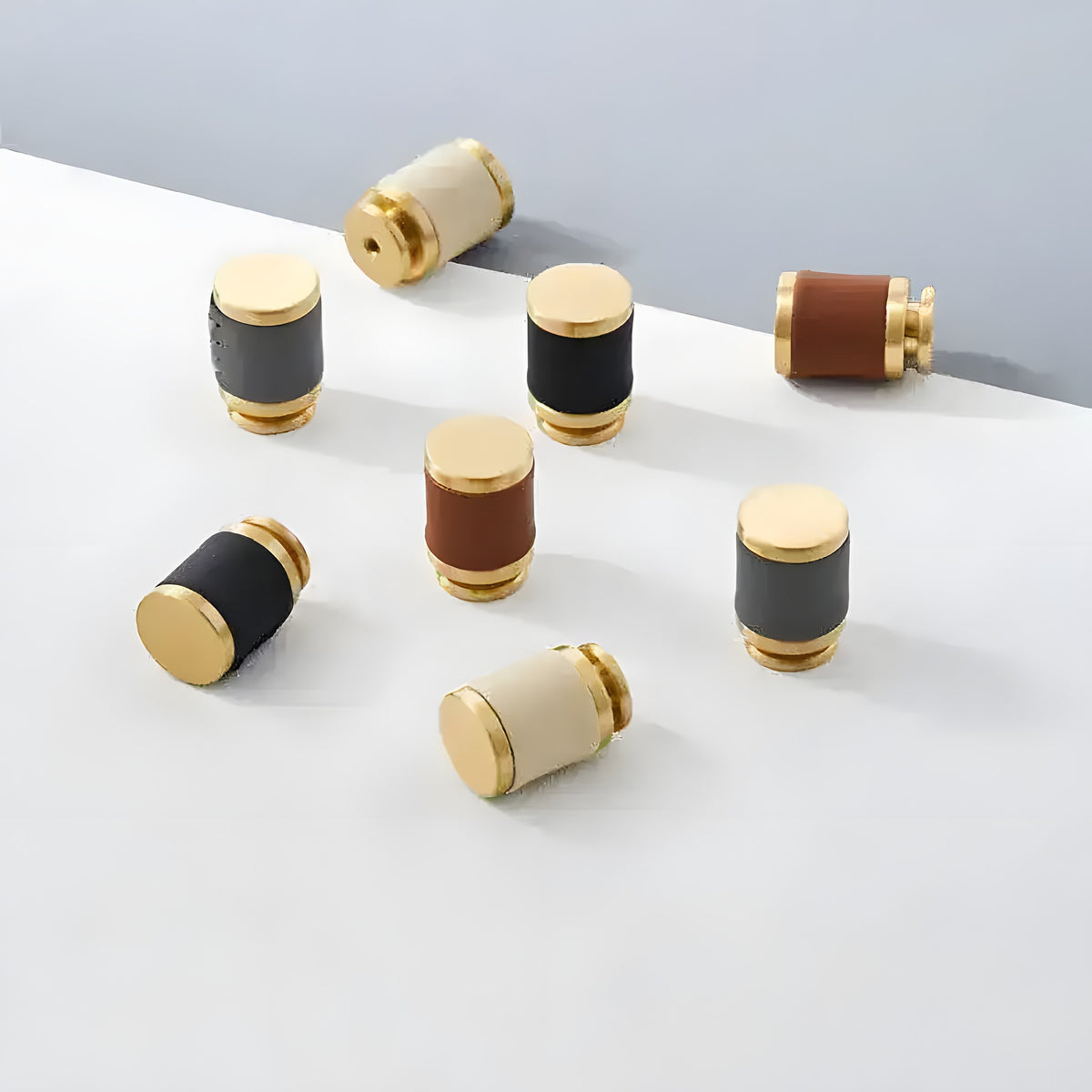 7 brass leather cabinet door knobs scattered on white surface in black, brown, and cream
