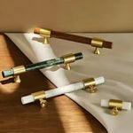 Three Meg cabinet pulls (brown, green, white marble bars with brass caps) plus two knob variants displayed on wood surface