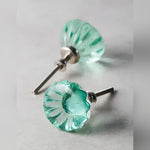 Two translucent green glass flower-shaped cabinet knobs with silver screw hardware on grey surface