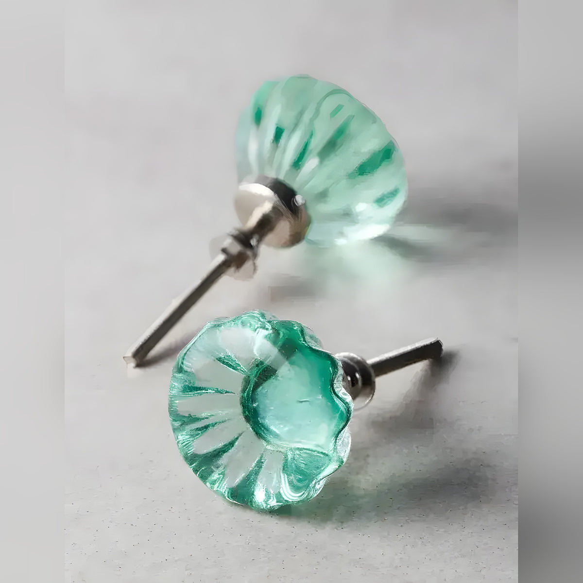 Two translucent green glass flower-shaped cabinet knobs with silver screw hardware on grey surface