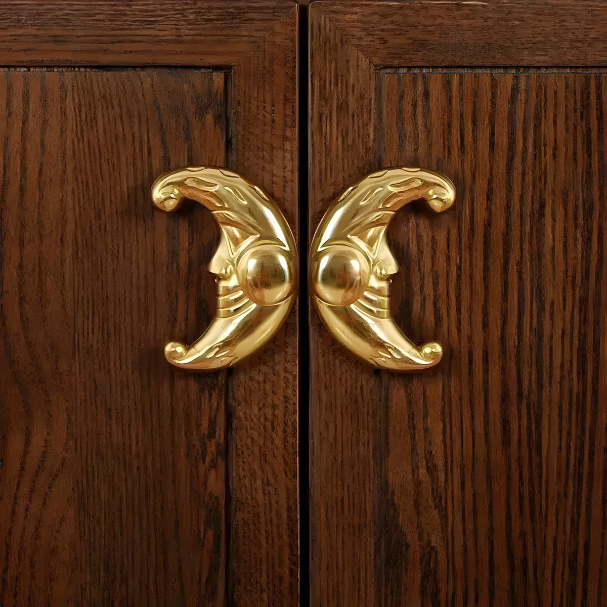 Two brass crescent moon-face drawer knobs mounted facing each other on dark oak cabinet doors