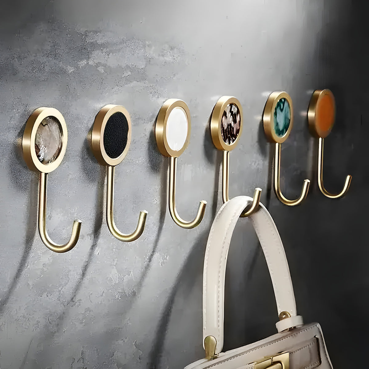 Six brass shell wall organizer hooks with colorful inlay centers mounted on concrete wall, handbag hanging from one