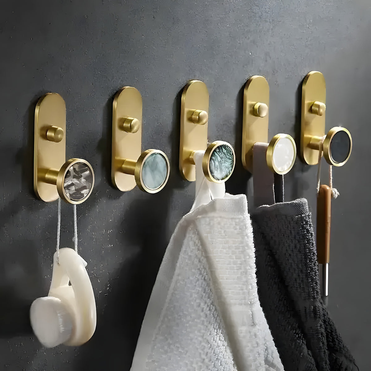 5 brass shell wall organizing hooks in a row on dark wall holding towels and earphones