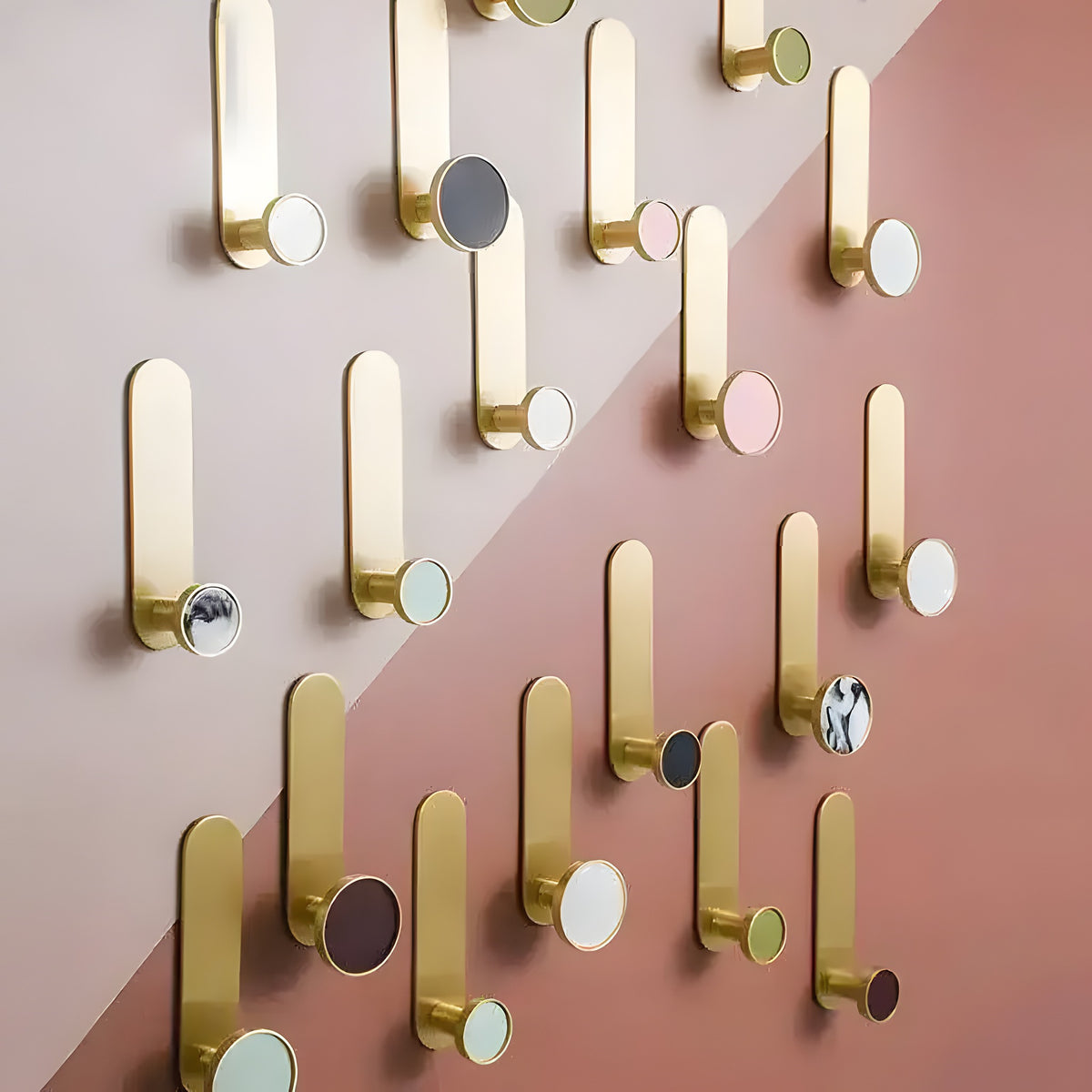 Multiple brass wall hooks with circular colored shell accents in pink, gray, marble, and white on two-tone pink wall