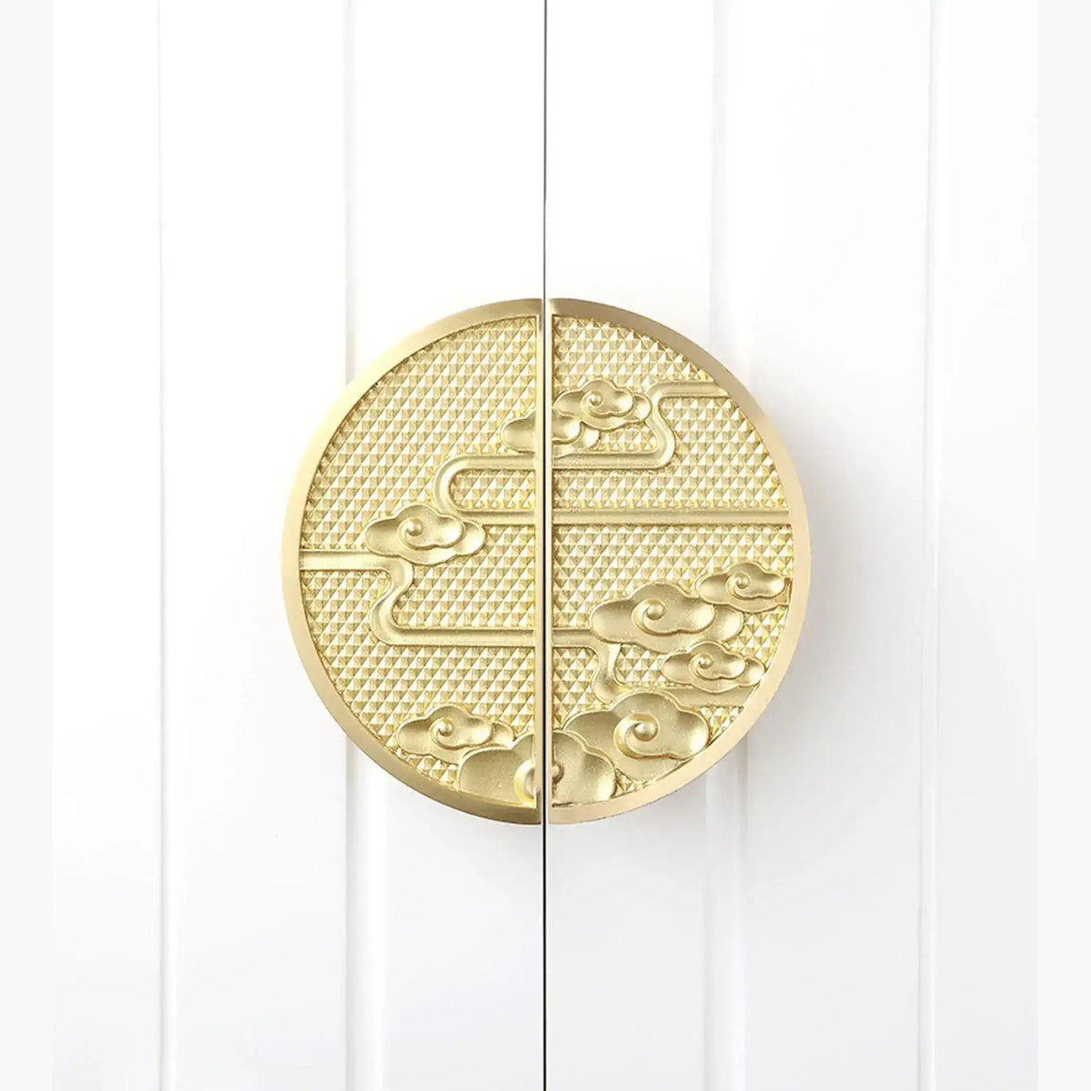 Two round brass chinoiserie knobs on white paneled cabinet doors face-on with cloud-wave relief pattern