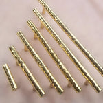 Five hammered brass cabinet drawer pulls in graduated sizes arranged diagonally on pink surface