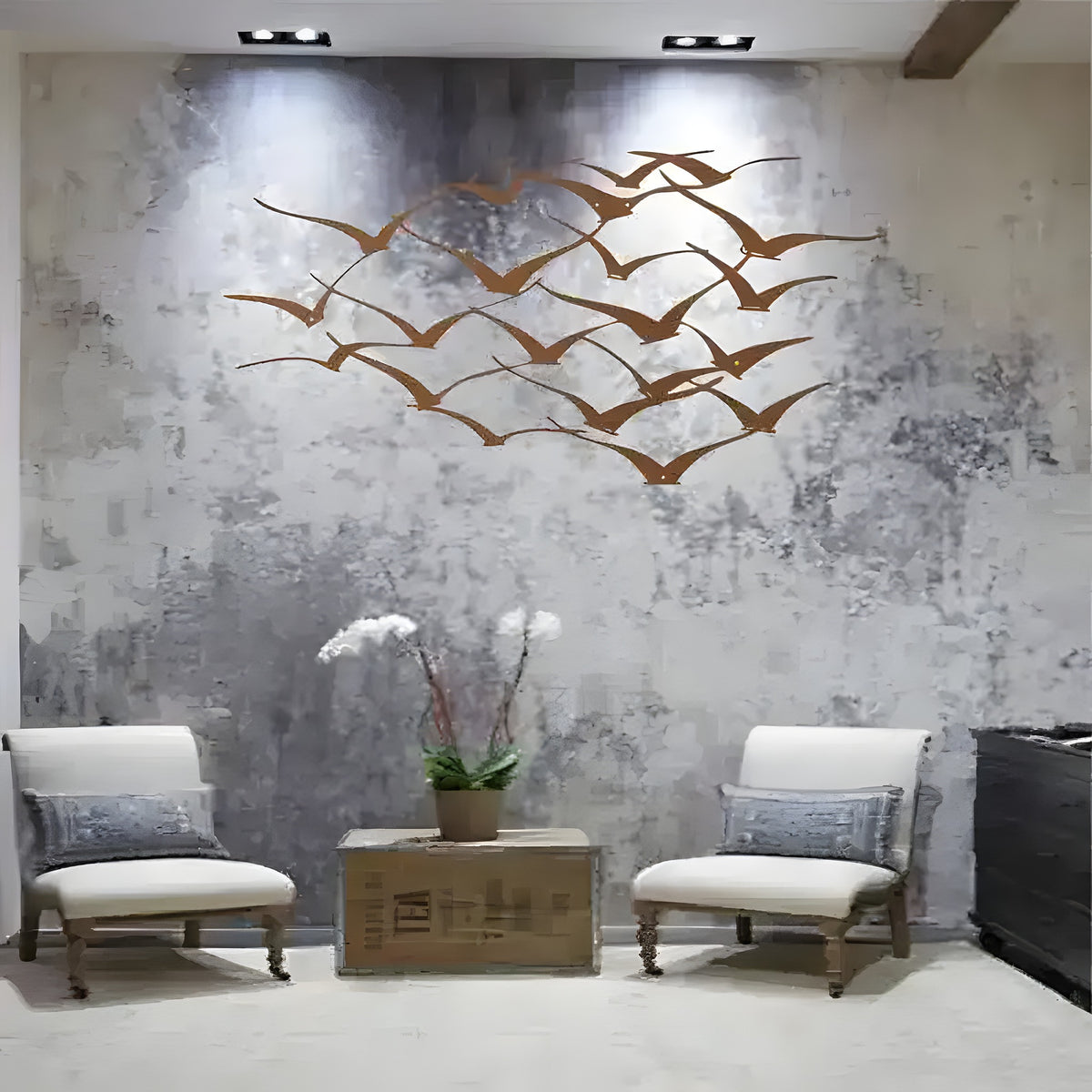 Bronze flying cranes metal wall art on textured concrete wall above two white armchairs and orchid centerpiece