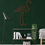 Copper-tone geometric flamingo metal wall art on dark green wall above open shelf with books and trailing plant