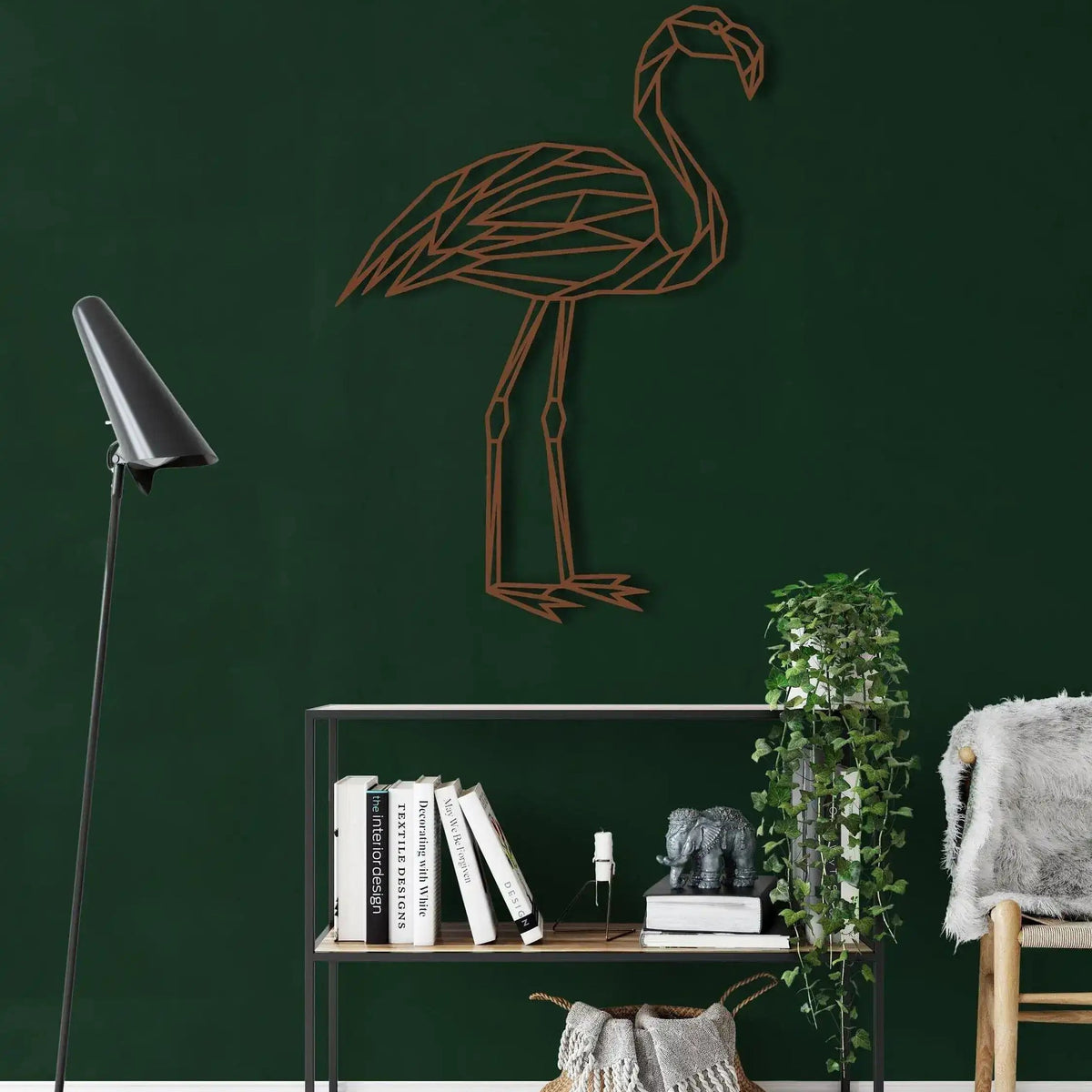 Copper-tone geometric flamingo metal wall art on dark green wall above open shelf with books and trailing plant