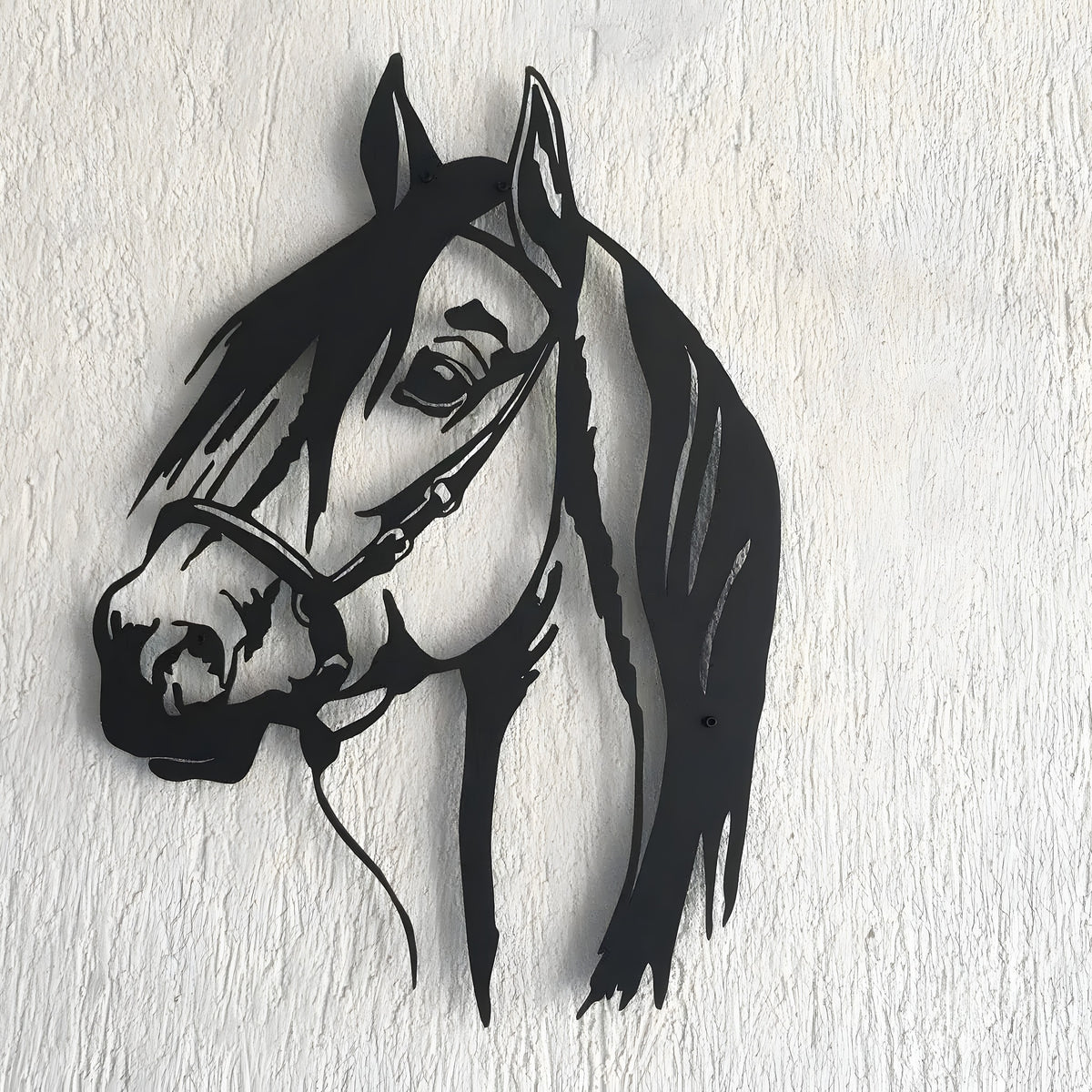 Black horse head metal wall hanging with bridle and flowing mane on white textured wall