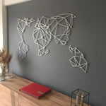 Silver geometric world map metal art on gray wall above a wooden sideboard with pampas grass