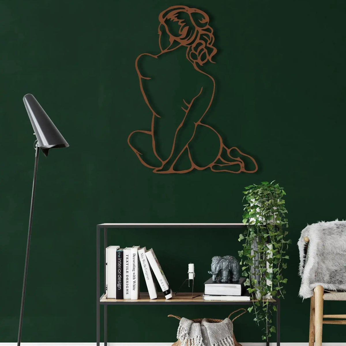Copper line-art diva woman silhouette seated with back turned, dark green wall above open metal shelf with ivy