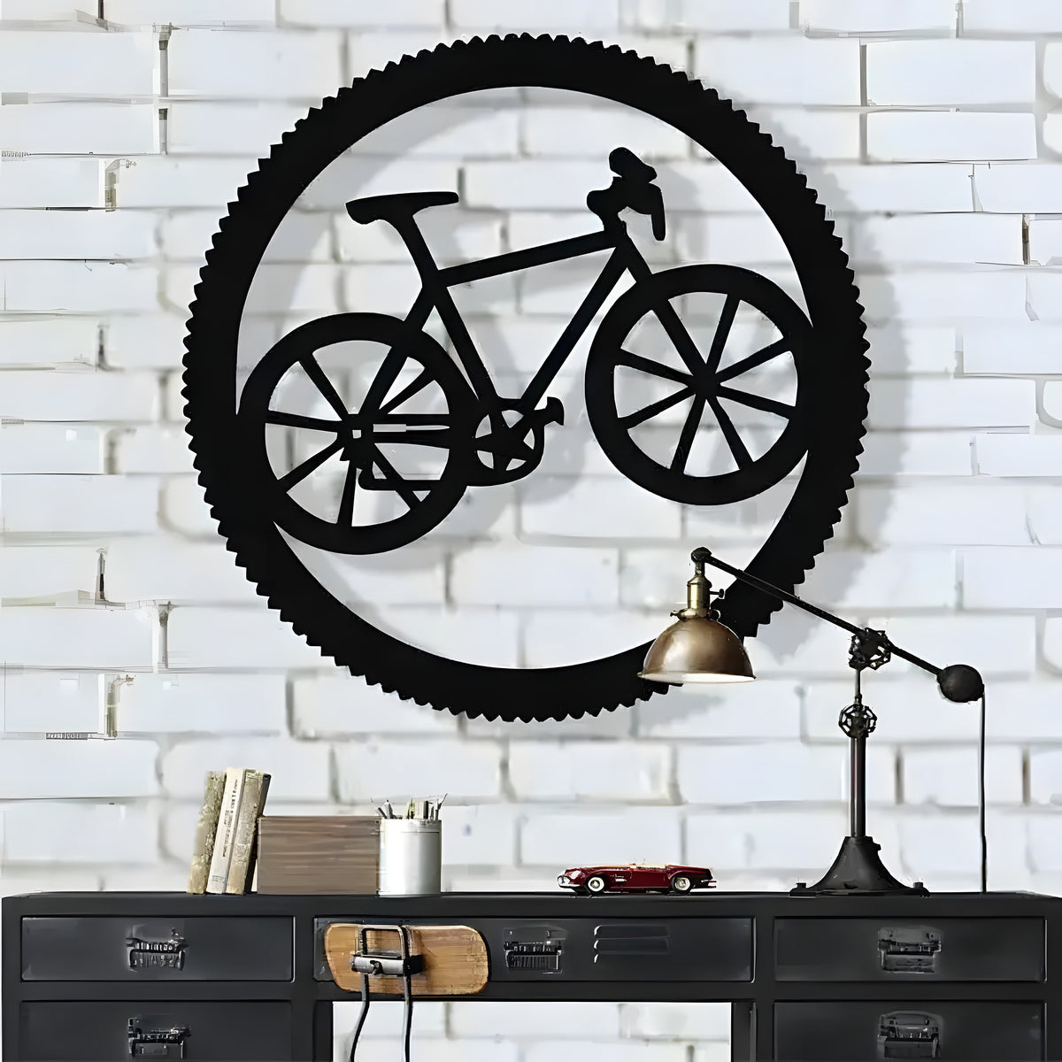 Black bicycle in circle metal wall art on white brick wall above dark industrial drawer unit and brass lamp
