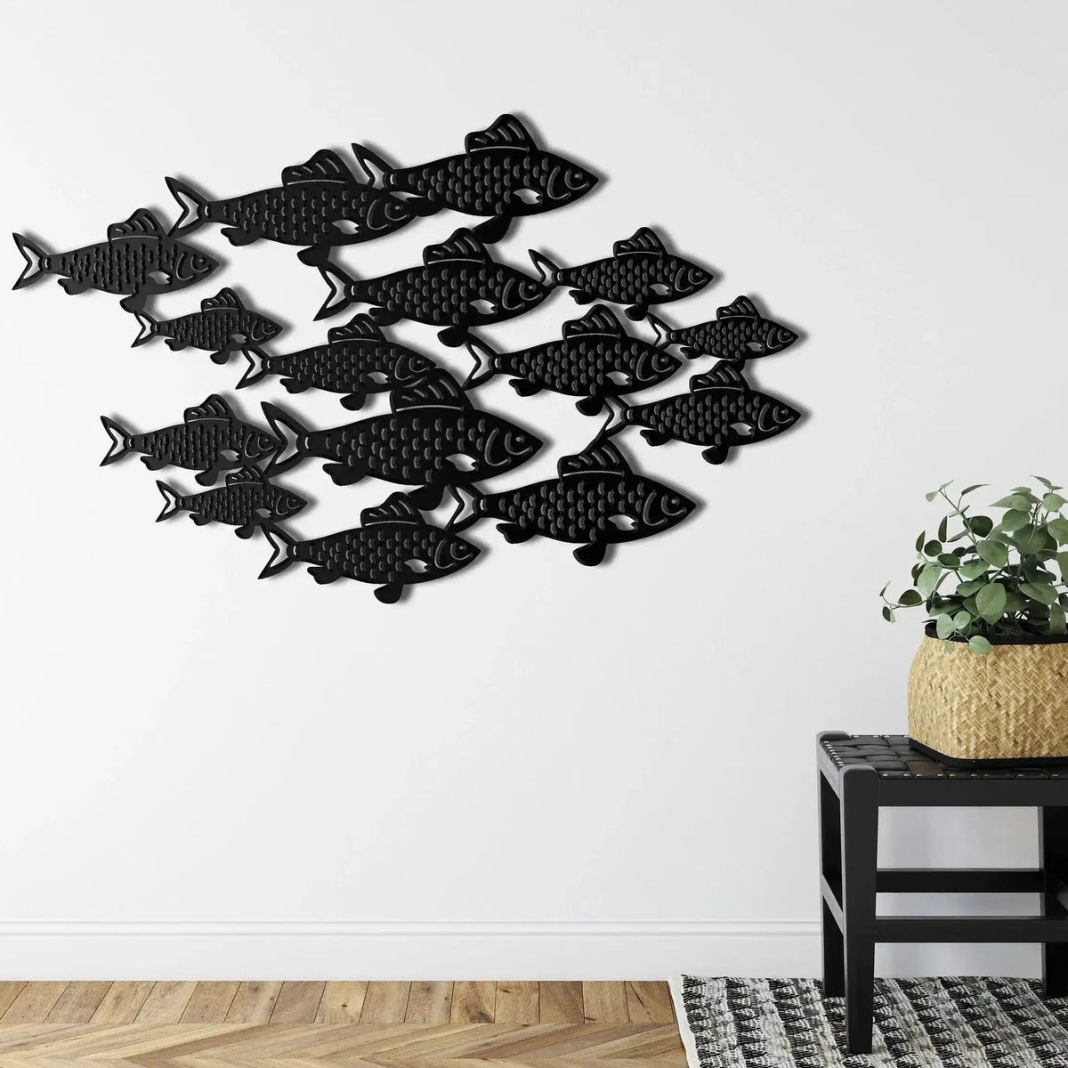 Black fish shoal metal wall art with school of fish on white wall above wicker stool with plant