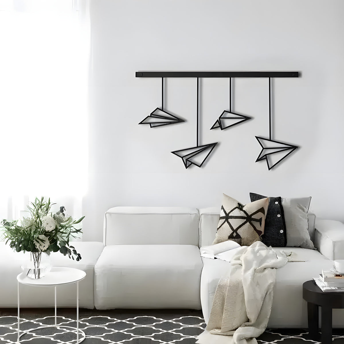 Black Paper Plane hanging wall art with four wire-frame planes from a rod, white wall above grey sofa